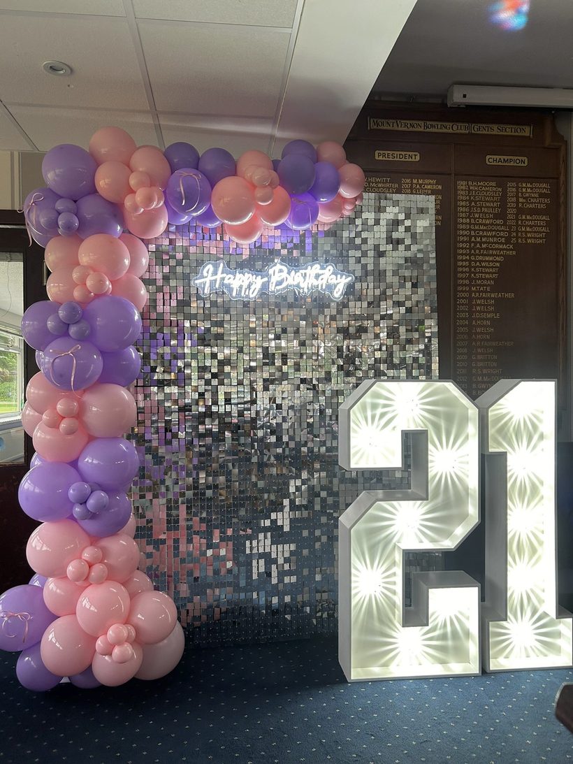 Light-up 21 numbers beside a sequin wall and pastel balloons